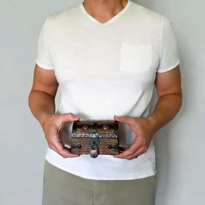 Shows the chest held in a real person's hands to convey its handheld size and rustic look.