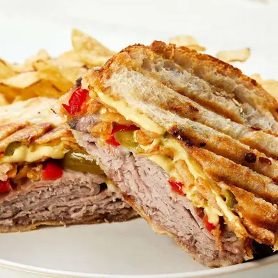 Shows the mustard used in a pressed sandwich to demonstrate its use as a sandwich condiment. Presents a real-world serving context with no text overlay to show appetizing use.