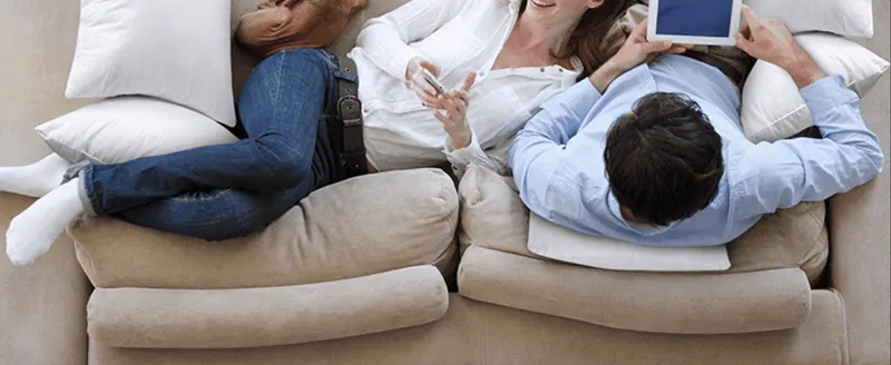 Shows people relaxing on a pillow-filled couch to help shoppers picture the product in a real, comfortable home setting.